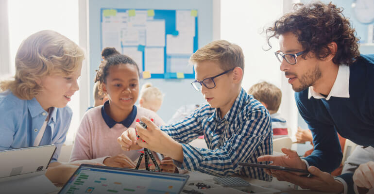 Two students work on a hands-on STEM project in front of a STEM teacher.