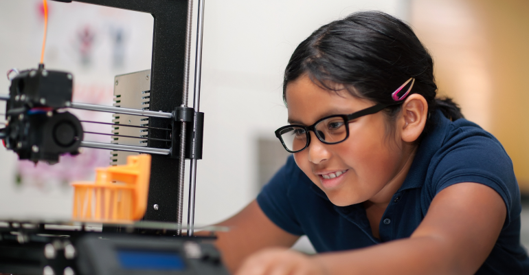 Young girl with glasses leaning in to a 3D printing as it prints.